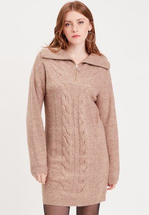 Robe-pull en tricot torsadé couleur brun clair, avec un col montant zippé, des manches longues et des poignets côtelés. Matière douce et texturée.
