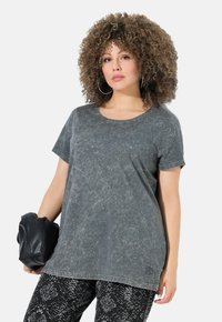 T-shirt grigio a maniche corte con un aspetto tessurizzato e sbiadito. Presenta un collo rotondo e un logo discreto vicino all'orlo. Abbinato a pantaloni a fantasia.