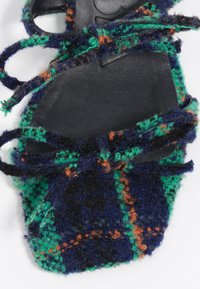 Sandalia plana con tiras que presenta una parte superior tejida a cuadros en azul marino, verde y naranja con una superficie texturizada y una suela negra. Cierres ajustables con lazos.