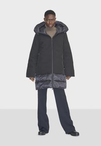 Čierny dlhý kabát so trblietavým šedým puffy spodným dielom, s veľkou kapucňou, zipsom vpredu a bočnými vreckami. Hladká látka s matným vrchom.