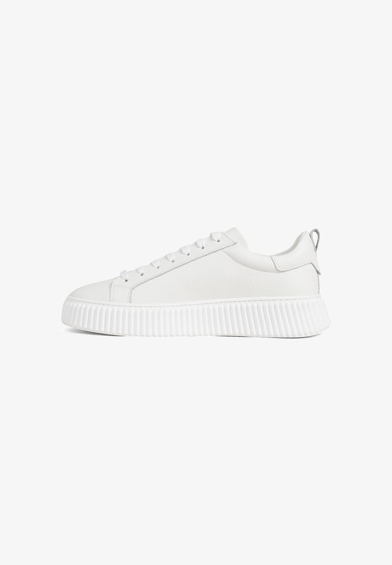 Witte lage sneaker met vetersluiting aan de voorkant en een dikke, geribbelde zool, zijaanzicht op een witte achtergrond.