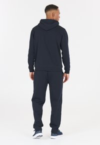 Mörkblå hoodie och matchande joggers i ett jämnt tyg. Huva design, elastiska ärmslut och midjeband, med detaljerad sömnad.