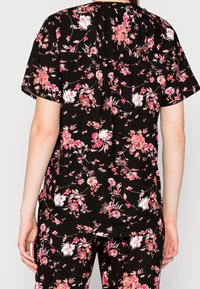 Floral print blouse with short sleeves, featuring a black background and multicolored flowers. The fabric has a soft texture and a relaxed fit.
