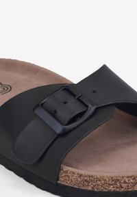 Sandale glissante en cuir noir avec une large sangle et une boucle réglable, dotée d'une semelle intérieure en liège marron rembourrée et d'une semelle noire texturée.