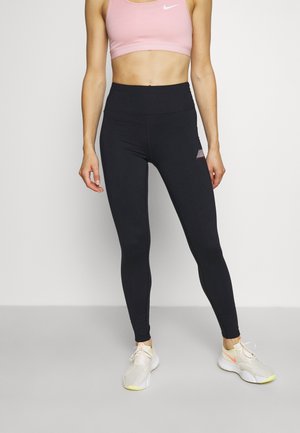 Black leggings with high waist, smooth texture, and a small graphic accent. Paired with a light pink sports bra. Athletic shoes with mesh detail.
