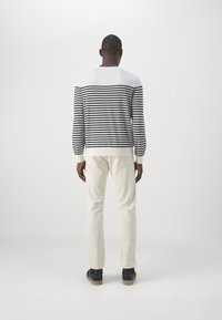 Suéter de rayas en blanco y negro con cuello redondo, combinado con pantalones beige y zapatos negros. Textura suave y diseño ajustado.