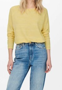 Pull rayé jaune à manches longues associé à un jean bleu taille haute avec une texture usée et des détails de couture visibles.