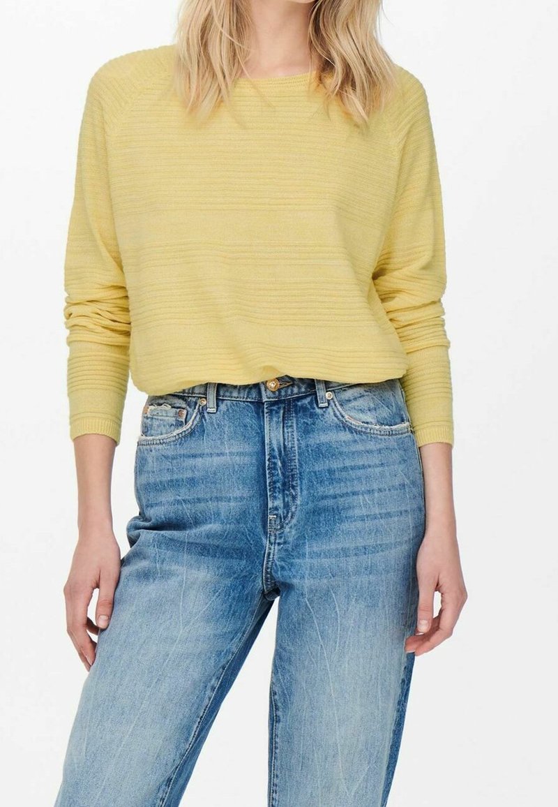 Pull rayé jaune à manches longues associé à un jean bleu taille haute avec une texture usée et des détails de couture visibles.