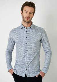 Lichtblauw button-up shirt met een geometrisch marineblauw patroon. Lange mouwen, kraag en zwarte knopen. Gemaakt van een gladde stof.