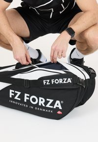 Mustan duffel-laukun valkoisilla yksityiskohdilla, jossa on "FZ FORZA" -brändäys, vetoketjusuljenta ja säädettävä olkahihna. Kangas näyttää kestävältä ja siinä on teksturoitu pinta.