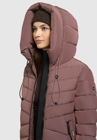 Polstret jakke i dæmpet mauve med en stor hætte, justeable snore, sidelommer med lynlås og en struktureret detalje på stoffet.