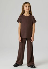 Brązowy prążkowany dzianinowy t-shirt z krótkimi rękawami i dopasowanymi szerokimi spodniami, zestawiony z czarnymi butami na masywnej podeszwie. Prosty, luźny design.