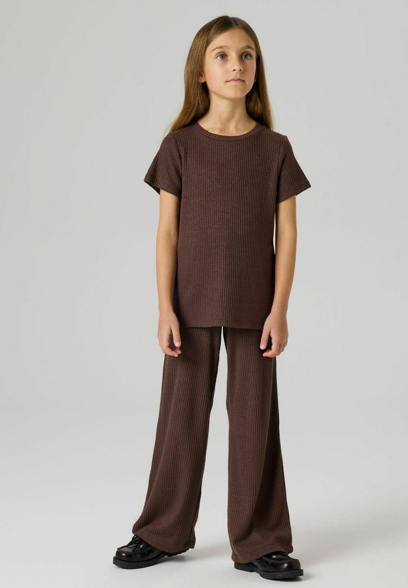 Brązowy prążkowany dzianinowy t-shirt z krótkimi rękawami i dopasowanymi szerokimi spodniami, zestawiony z czarnymi butami na masywnej podeszwie. Prosty, luźny design.