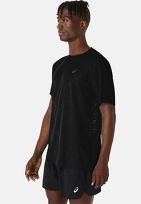 Schwarzes sportliches T-Shirt mit kurzen Ärmeln, mit einem strukturierten Muster und einem kleinen Logo auf der Brust. Leichtes, atmungsaktives Gewebe.