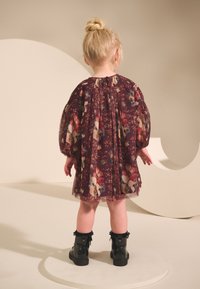 Violetas kleita ar ziedu rakstu, pūkainām piedurknēm, caurspīdīgu audumu un sanestu apkakli, kas savienota ar spīdīgām melnām potīšu zābakām.