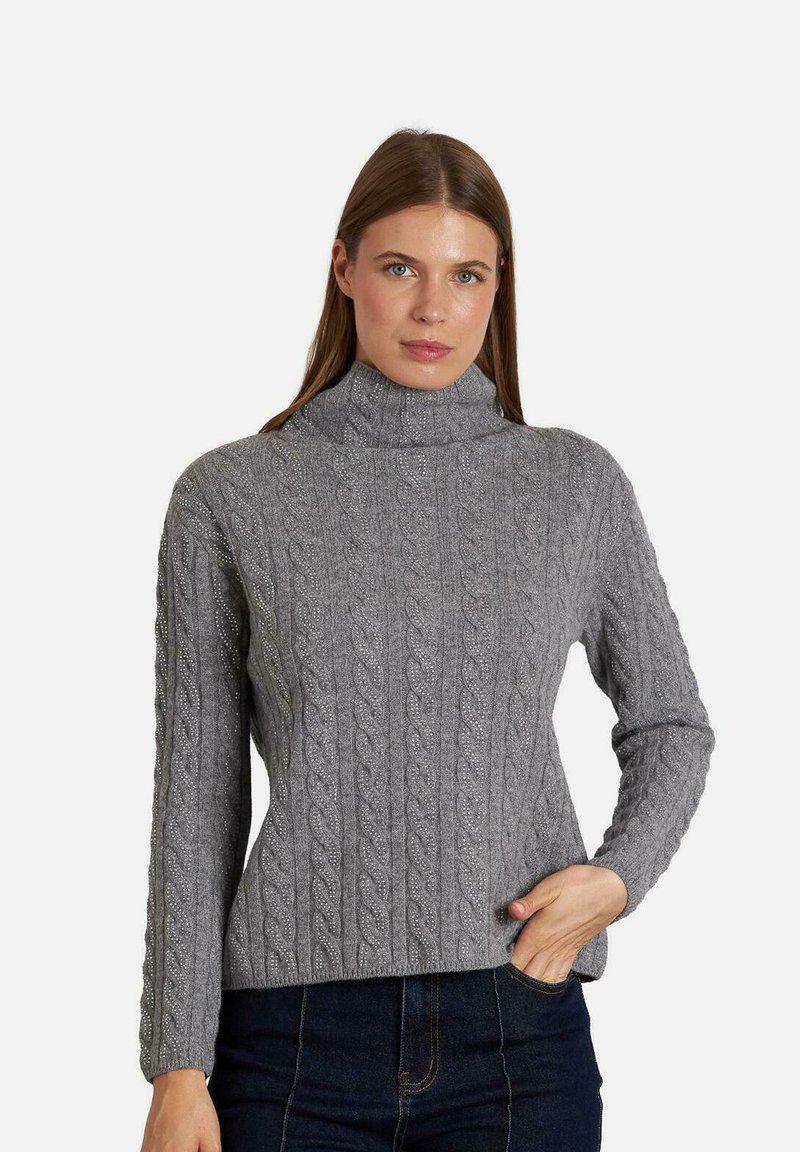 Maglione grigio a maglia intrecciata con un alto collo, caratterizzato da motivi testurizzati e maniche lunghe, abbinato a jeans in denim scuri.