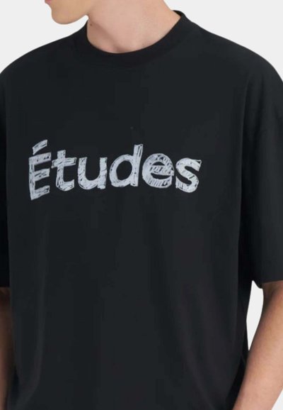 Personne portant un t-shirt noir à manches courtes avec le mot « Études » en texte blanc stylisé sur la poitrine.