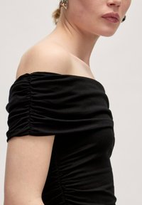 Zwarte off-shoulder top met geplooide stof bij de mouwen en zijkant, gemaakt van een zachte, rekbare stof. Glad textuur, aansluitend ontwerp.