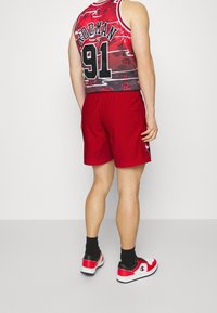 Röda basketshorts tillsammans med en svart och röd grafiklinne som har mönster och siffran 91. Svarta och röda sneakers med vit sula.