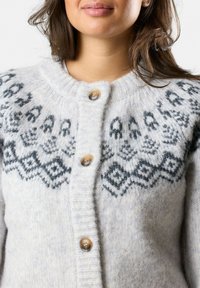 Cardigan grigio a maglia realizzato in lana, con scollo rotondo, chiusura con bottoni prominenti e un motivo geometrico nero sulla parte superiore.