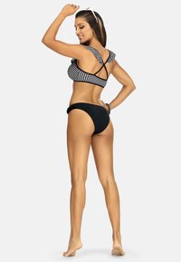 Czarny i biały bikini w kratkę z falbaniastymi ramiączkami, zestawione z czarnymi majtkami o teksturowanej talii i minimalnym zakryciu.