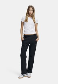 Svart joggebukser med en avslappet passform, paret med en tettsittende hvit t-skjorte. Joggebuksene har snøring i livet og sid lommer, sammen med hvite sneakers.