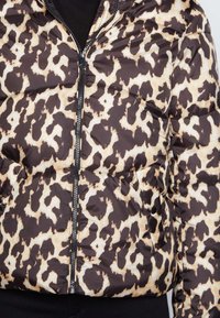 Chaqueta tipo puffer con un estampado de leopardo negro y beige, que cuenta con cremallera frontal, bolsillos laterales y textura acolchada. Material suave y ligero.