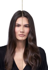 Portrait d'une personne avec de longs cheveux ondulés et foncés, portant un haut noir. Une ligne pointillée divise le visage verticalement, révélant des traits symétriques.