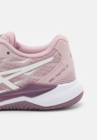Zapatilla deportiva rosa con parte superior de malla texturizada, acentos blancos y suela morada. Presenta un talón reforzado y un diseño lateral con patrón.