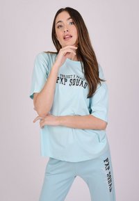 Camiseta oversized de color azul claro con texto en blanco y negro "PROJECT X PARIS PXP SQUAD," combinada con pantalones de color azul claro a juego que presentan un texto similar.