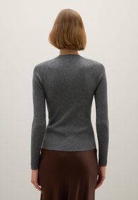 Grijze geribbelde lange-mouwen top met een ronde hals en een aansluitend ontwerp, gecombineerd met een gladde, bruine satijnen rok, gezien van achteren.