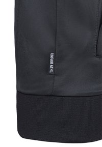 Pantaloni sportivi neri con una texture liscia, vita elasticizzata e un piccolo etichetta con la scritta "UNFAIR ATHL." stampata in bianco.