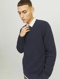 Marinblå stickad tröja med ett strukturerat mönster, rund halsringning och ribbade ärmslut. Bärs över en kragtröja med gräddfärgade ränder.