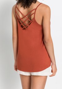 Top in tinta ruggine con un design a incrocio sulle spalle. Realizzato in materiale morbido con orlo arrotondato e spalline sottili.