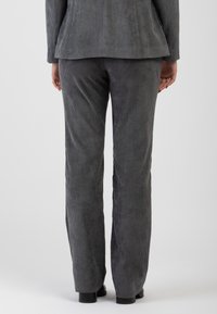 Pantaloni in corduroy grigi con una silhouette aderente, dotati di una texture a righe verticali, gambe dritte e piccole scarpe nere visibili all'orlo.