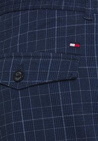 Námořnická modrá kostkovaná košile s texturovanou bavlněnou směsí, bílými a světle modrými pruhy, kapsou na klopu a černým knoflíkem s logem.