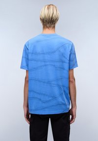 T-shirt blu a maniche corte con una texture a onde, realizzato in cotone. Presenta un collo rotondo e una vestibilità rilassata, con orlo dritto.