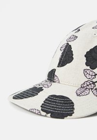 Cap with a cream fabric featuring black floral patterns and light pink leaves, structured design, and a curved brim.