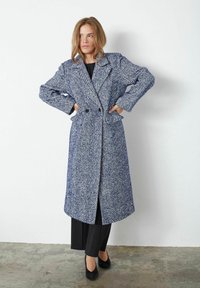 Dolga plašč s houndstooth vzorcem v odtenkih modre in bele, z dvojno zapenjanjem, širokimi reverji in stranskimi žepi.