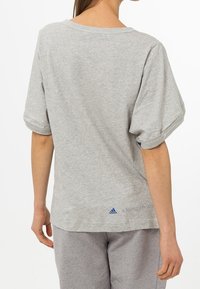 Šedé, krátké tričko s uvolněným střihem vyrobené z bavlny. Má ohrnuté rukávy a modré logo "Stella McCartney" a Adidas na zádech.