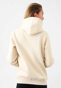 Felpa beige con un grande cappuccio, polsini e orlo a costine. Tessuto liscio, vestibilità comoda e design minimalista. La vista posteriore mostra dettagli di cucitura.