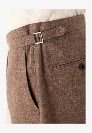 Brown tailored trousers made from textured fabric, featuring a silver buckle at the waist, pleats, and a back pocket with a button.