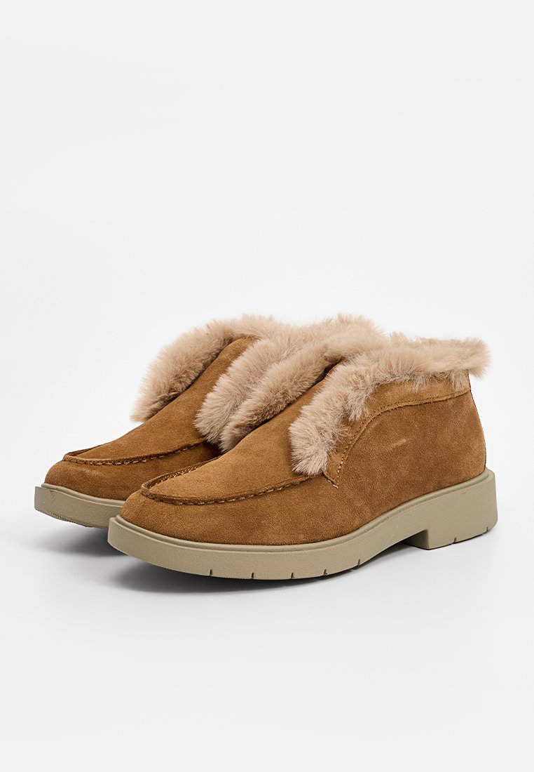 Bottines en suede marron avec un revers en fausse fourrure et une semelle en caoutchouc épaisse, présentant des pointes arrondies et de simples détails de couture.