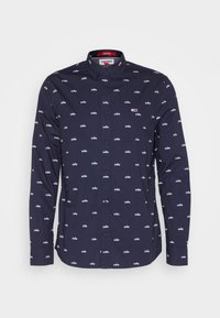 Granatowa koszula z długim rękawem zapinana na guziki z małymi białymi wzorami i małym logo Tommy Hilfiger w kolorach czerwonym, białym i niebieskim na klatce piersiowej.
