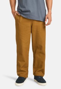 Pantaloni di cotone kaki con vestibilità rilassata, gambe dritte e una texture minimale. Abbinati a sneakers blu/neri e una maglietta grigia.