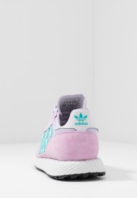 Baskets en daim rose avec rayures teal, accent logo blanc, talon texturé et semelle intermédiaire blanche ; la vue arrière met en valeur la forme et les matériaux utilisés.