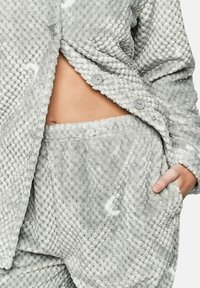Ensemble de lounge gris et texturé fabriqué à partir d'un tissu doux et pelucheux ; comprend un top à boutons avec deux boutons et un pantalon à taille élastique assorti avec des poches.