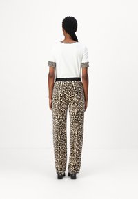 White t-shirt with leopard print cuffs, paired with loose-fitting leopard print trousers. Features a black elastic waistband and smooth texture.