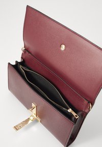 Borsa textured color bordeaux con chiusura in metallo dorato, dotata di una tasca interna con zip e di un rivestimento interno nero a contrasto.