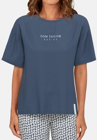 Blue short-sleeve t-shirt with a crew neck. Features white printed "TOM TAILOR EST. 62" logo on the front. Smooth fabric texture.
